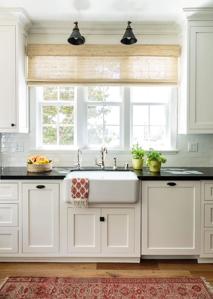 a kitchen with white cabinets and black counter tops, an area rug and two lights above the sink