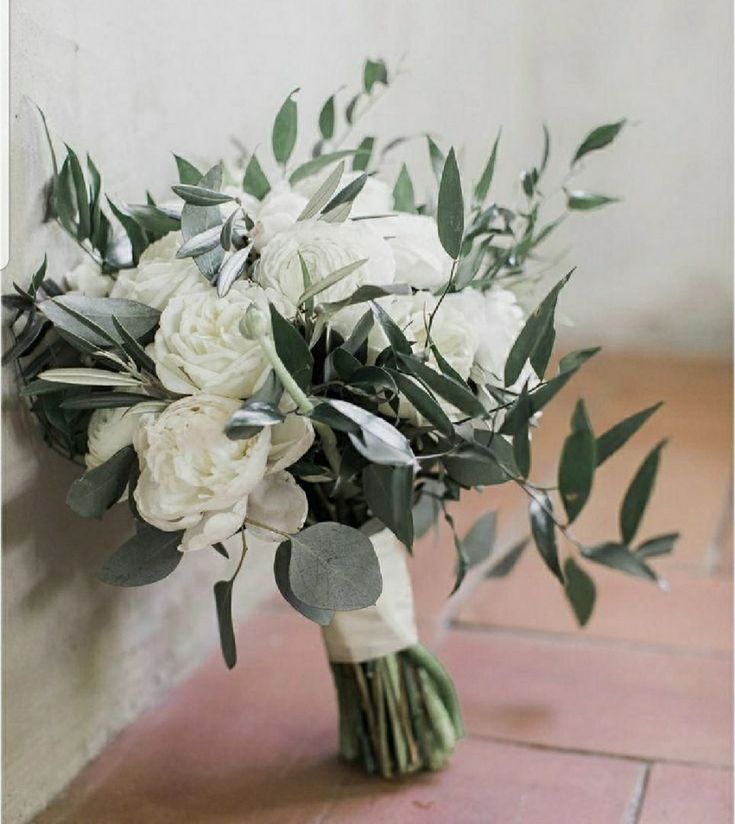 a bridal bouquet with white flowers and greenery on a brick floor in front of a wall