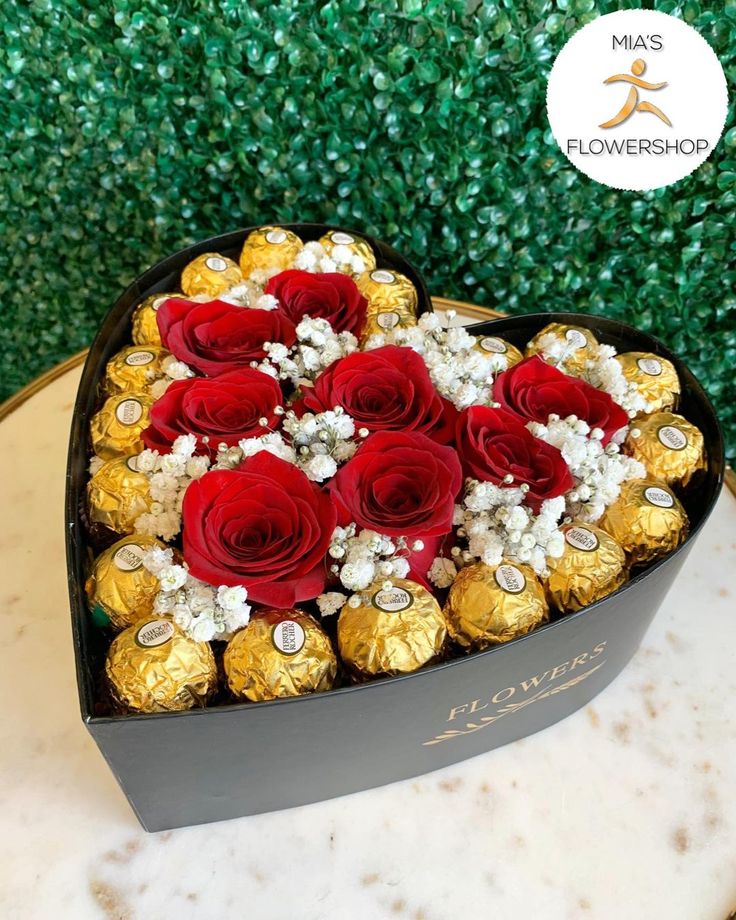 a heart - shaped box filled with chocolates and roses on top of a table