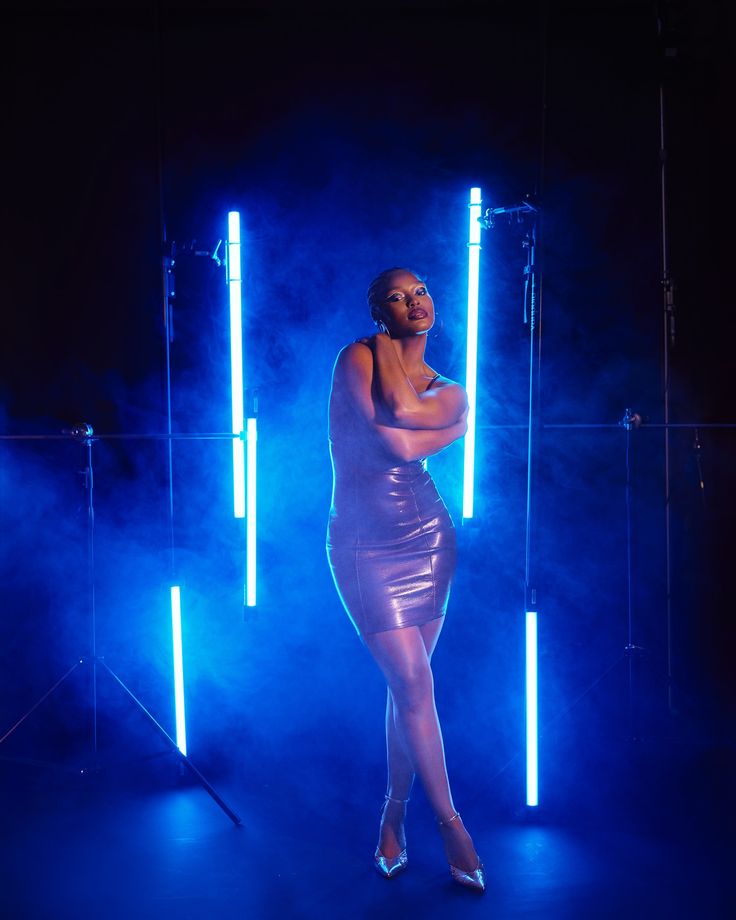 a woman standing in front of some blue lights with her hands on her hips and arms behind her back