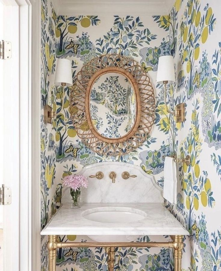 a white sink sitting under a mirror next to a wall covered in floral wallpaper