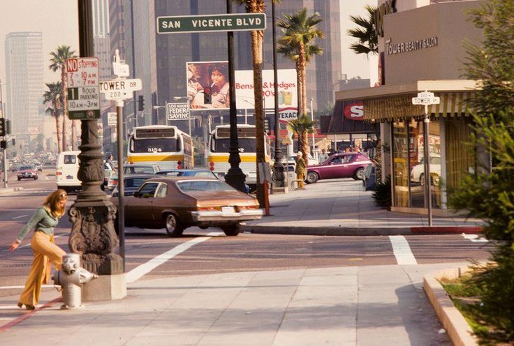 a woman sitting on a pole in the middle of a street with cars driving by