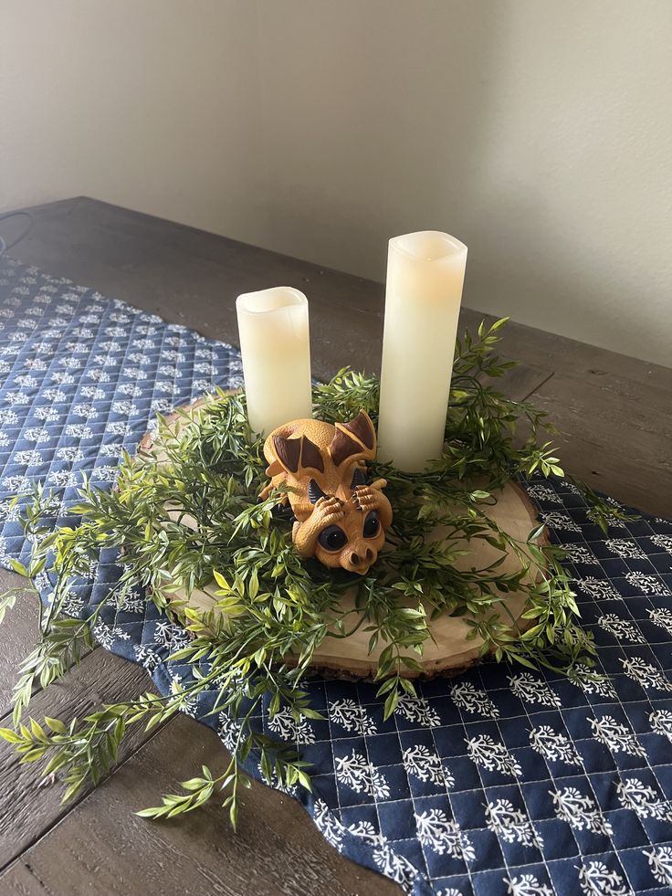 two candles sitting on top of a wooden bowl with greenery and leaves around it