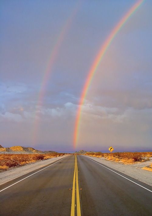 two rainbows are in the sky over an empty road with no cars on it