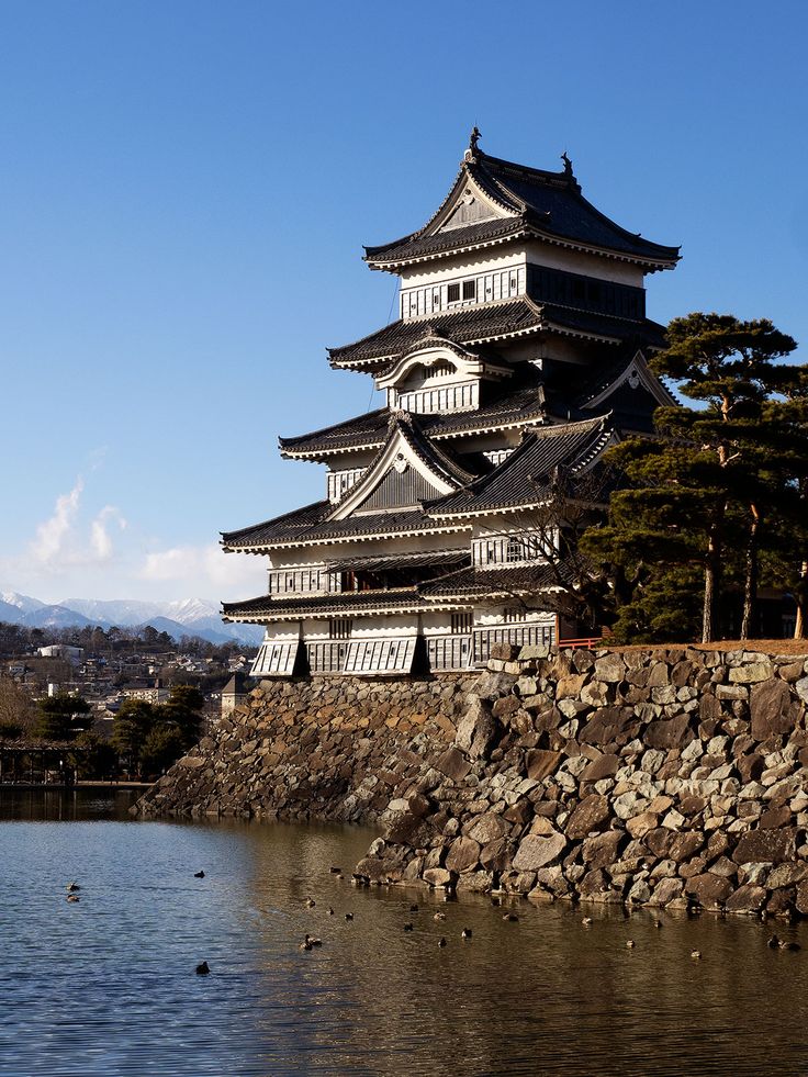 a tall building sitting on top of a lake next to a stone wall and trees