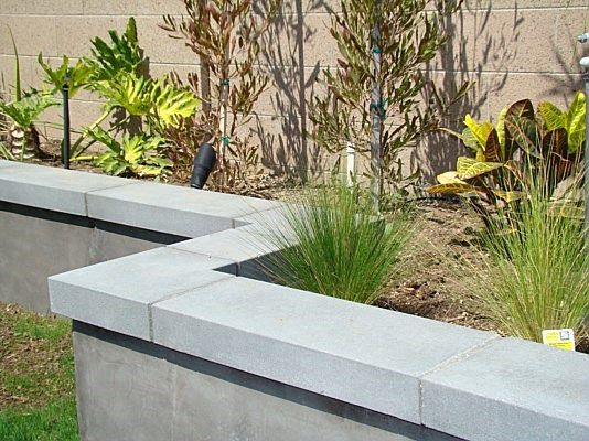 concrete planters are lined up in front of a brick wall with plants growing out of them