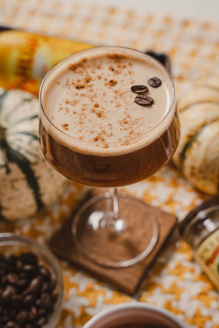 a drink in a glass sitting on top of a table next to some coffee beans