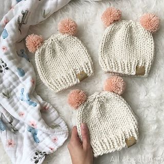 three knitted hats with pink pom poms on top, one in white and the other in beige