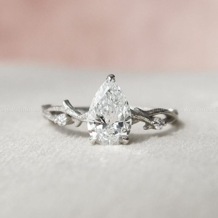 a white gold ring with a pear shaped diamond in the center and leaves around it