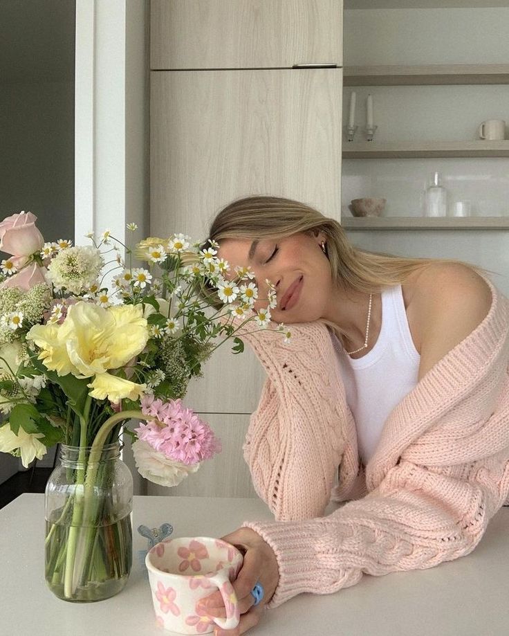 a woman sitting at a table with flowers in a vase next to her and looking down