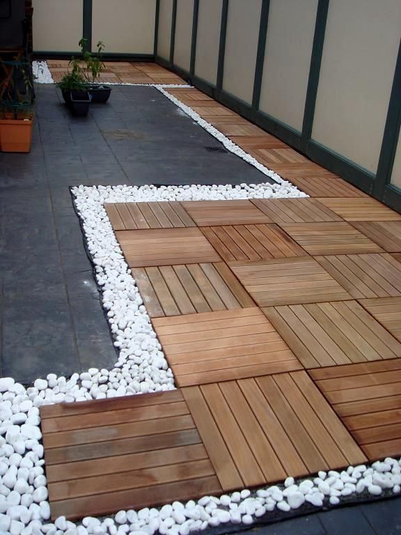 a wooden deck surrounded by white rocks and plants on the side of a building with glass doors