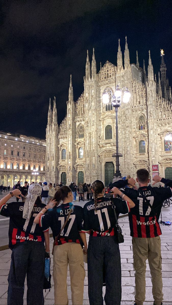 a group of people standing in front of a cathedral at night with their backs to the camera