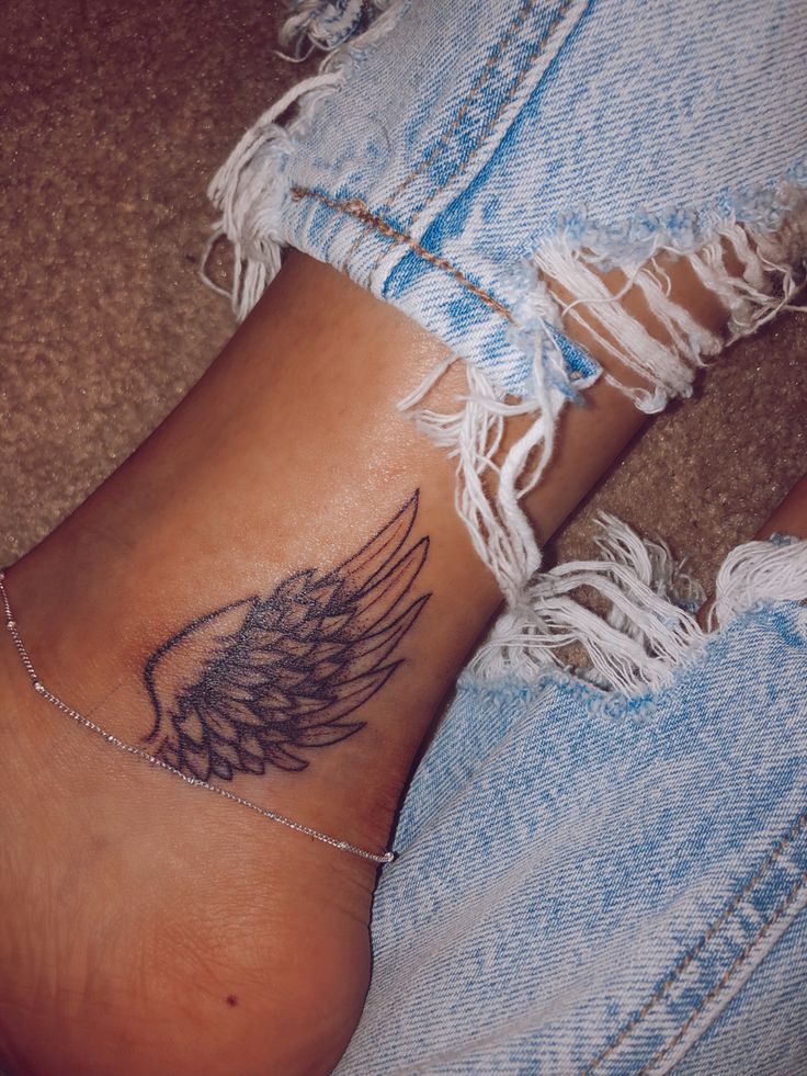 a woman's foot with an angel wing tattoo on the side of her leg