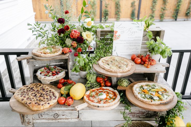 an assortment of pizzas are on display in front of some flowers and greenery