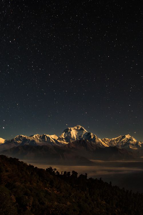 the night sky is lit up with stars above mountains and clouds in the foreground