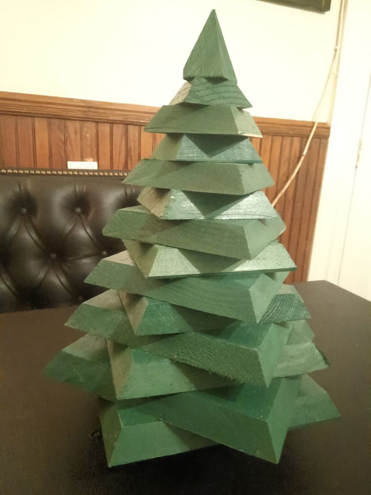 a green wooden christmas tree sitting on top of a table next to a brown leather chair