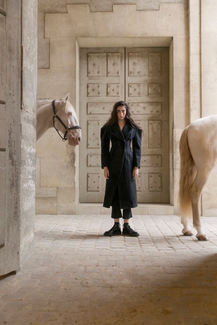 a woman standing next to a white horse in an enclosed area with stone walls and doors