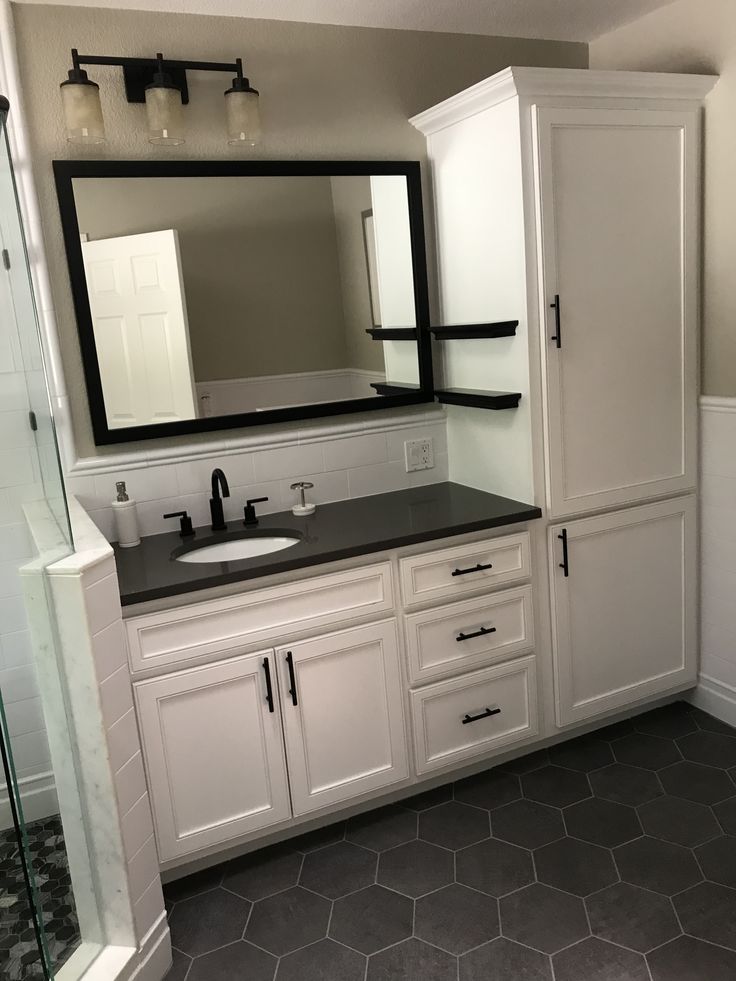 a bathroom with white cabinets and black counter tops on the sink, along with a large mirror