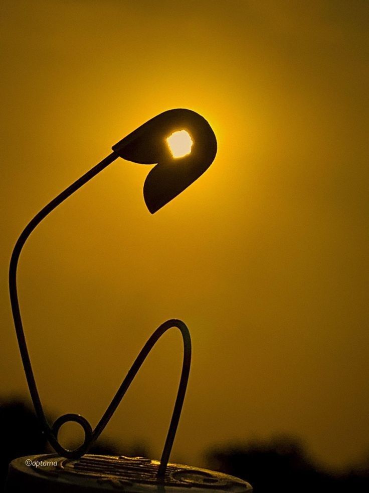 the sun is setting behind a lamp on top of a round object in front of a yellow sky