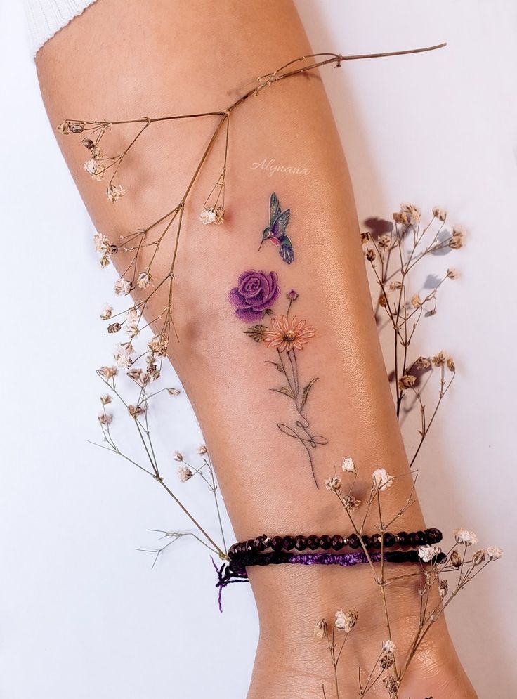 a woman's tattoo with flowers and butterflies on her leg, next to dried plants