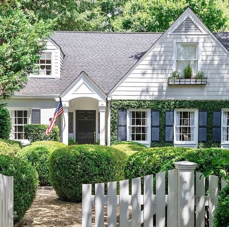 a white house with blue shutters and an american flag on the front door is shown