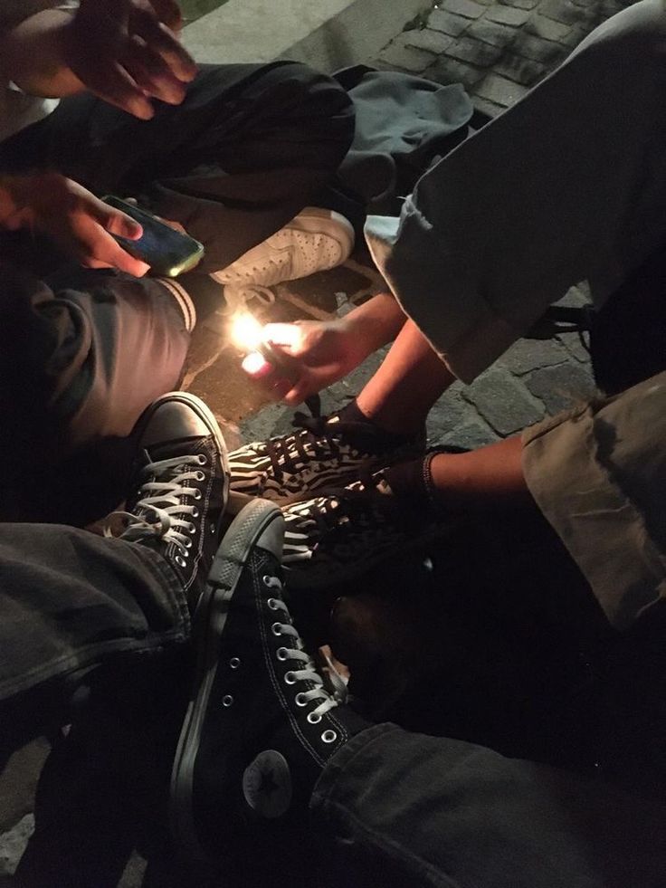 three people sitting on the ground with one holding a lit candle in their hand and another standing over them