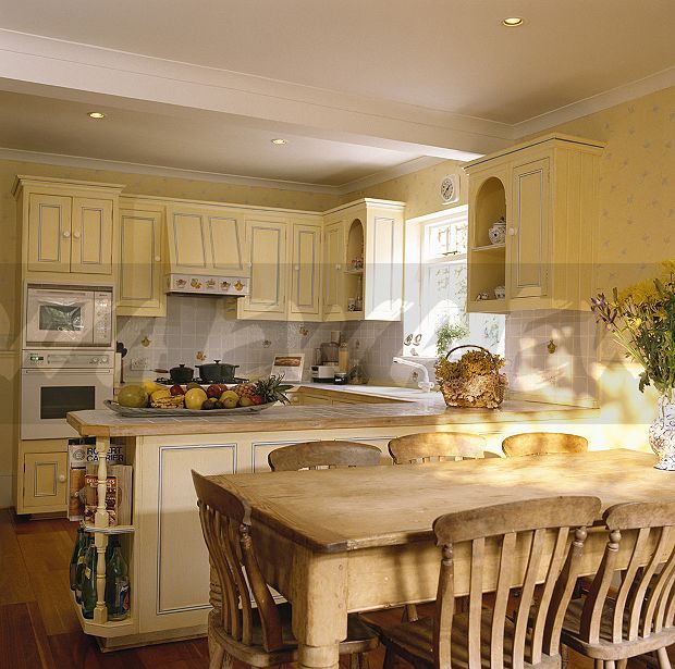 a large kitchen with yellow cabinets and wooden table surrounded by chairs in front of the counter