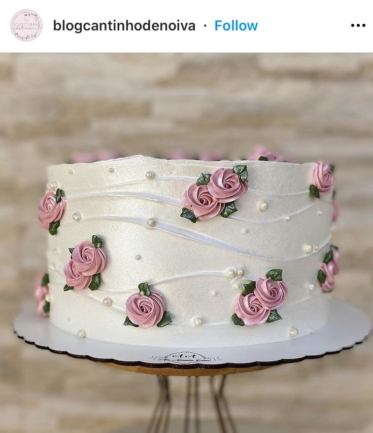 a white cake with pink roses on it sitting on a stand in front of a brick wall