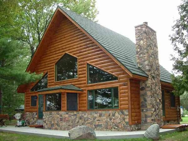 a log cabin with stone chimney and large windows