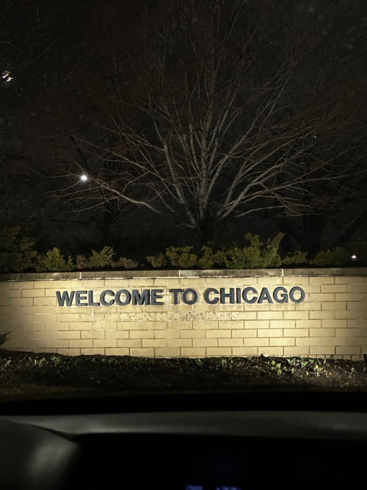 the welcome sign to chicago is lit up in front of a brick wall at night