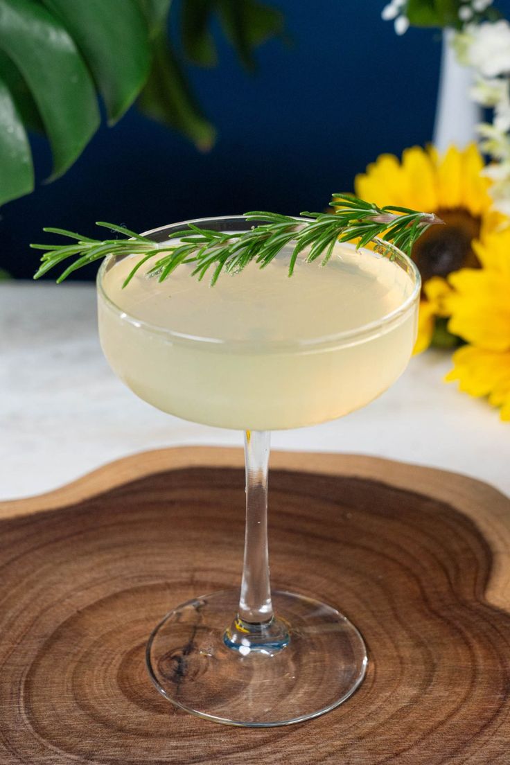 a drink in a coupe glass on a wooden tray with yellow flowers and greenery