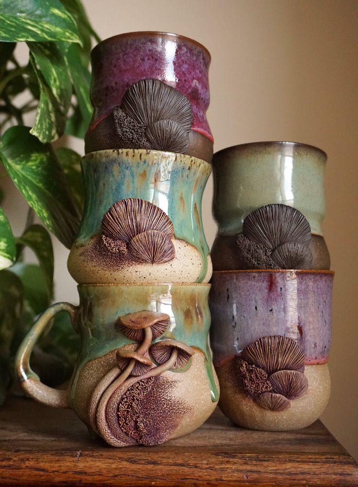 four ceramic mugs sitting on top of a wooden table next to a potted plant