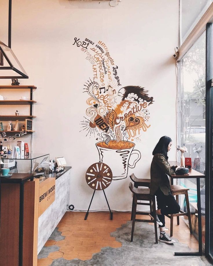 a woman sitting at a table in front of a wall with an artistic mural on it