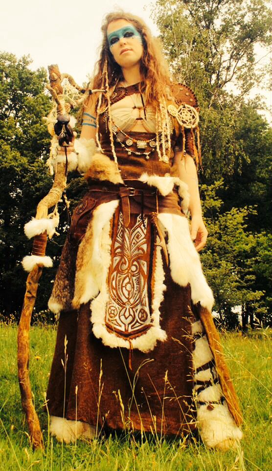 a woman dressed in native american clothing holding a stick