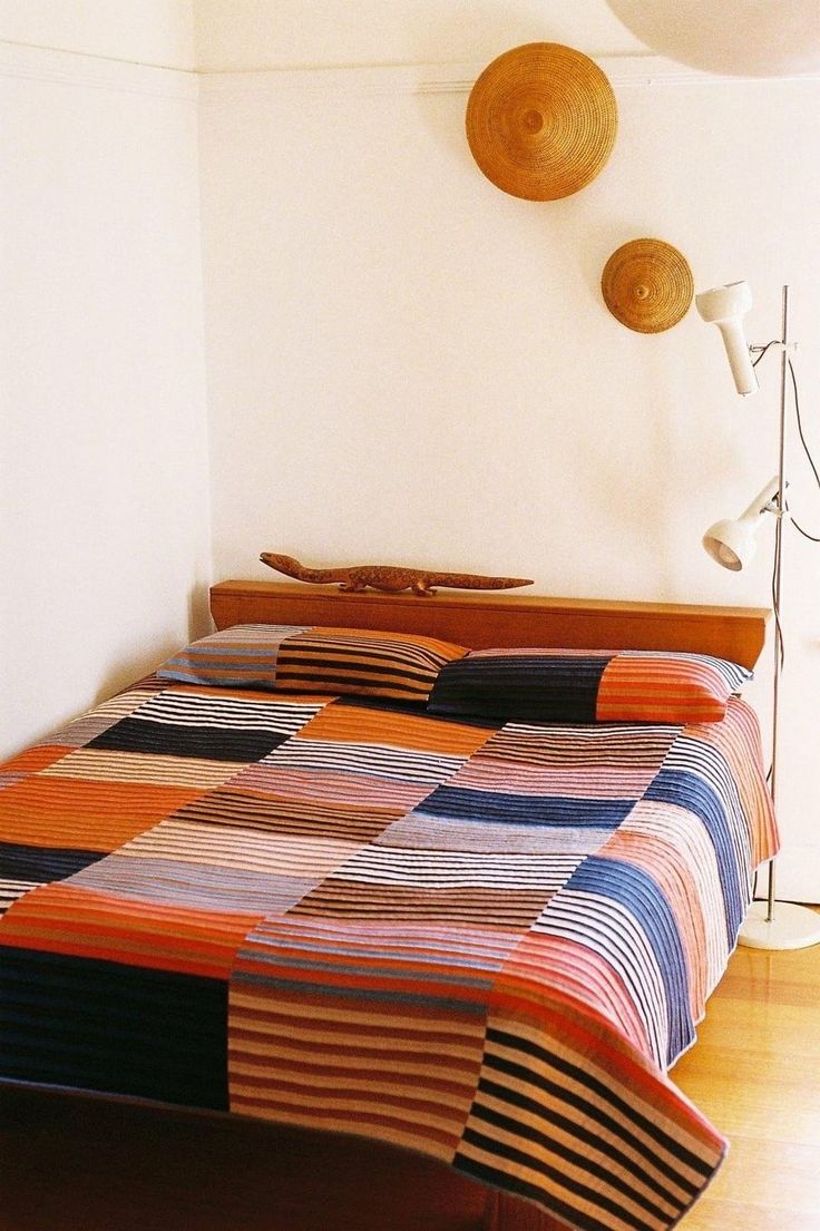 a bed with a colorful quilt on it and two lamps hanging above the headboard