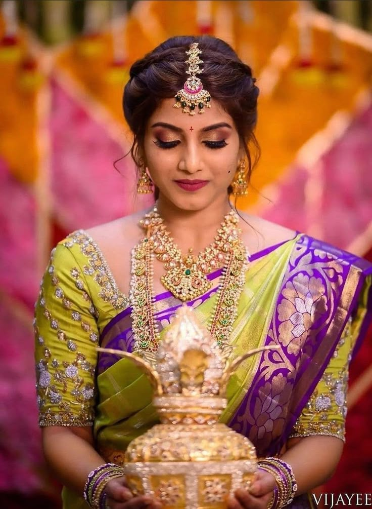 a woman in a green and purple sari holding a golden vase with jewels on it