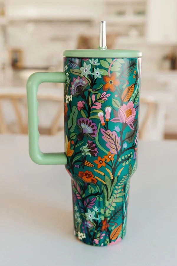 a green cup with floral designs on it sitting on a table in front of a dining room