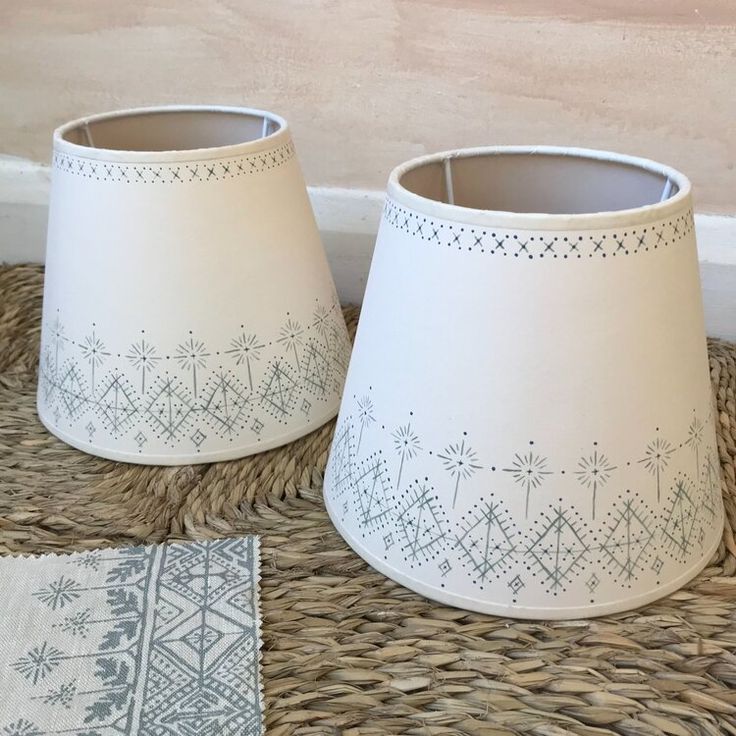 two white lampshades sitting on top of a wicker table cloth next to each other