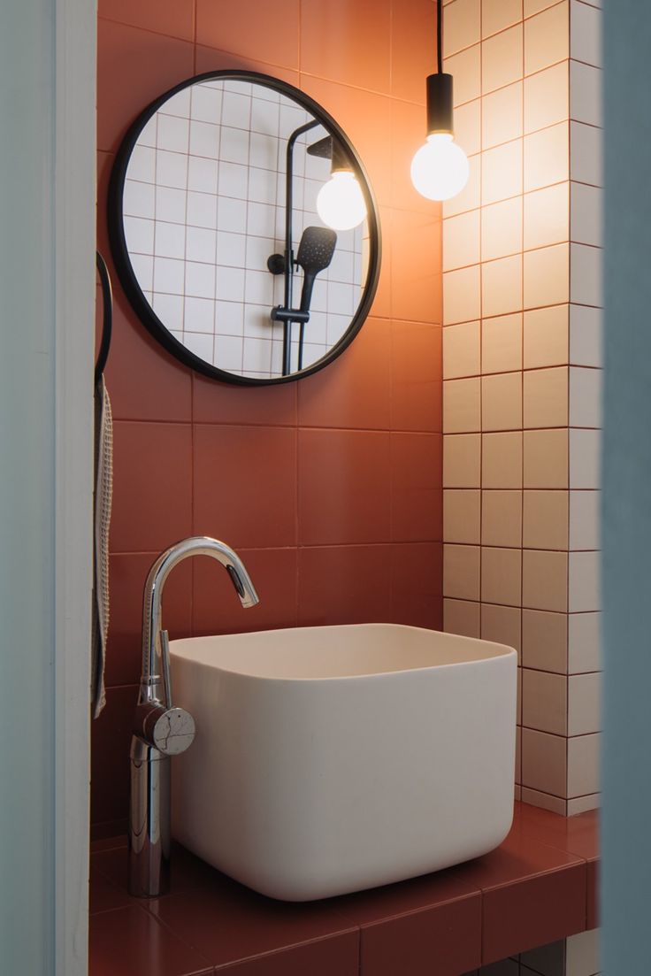 a bathroom sink sitting under a round mirror next to a wall mounted faucet