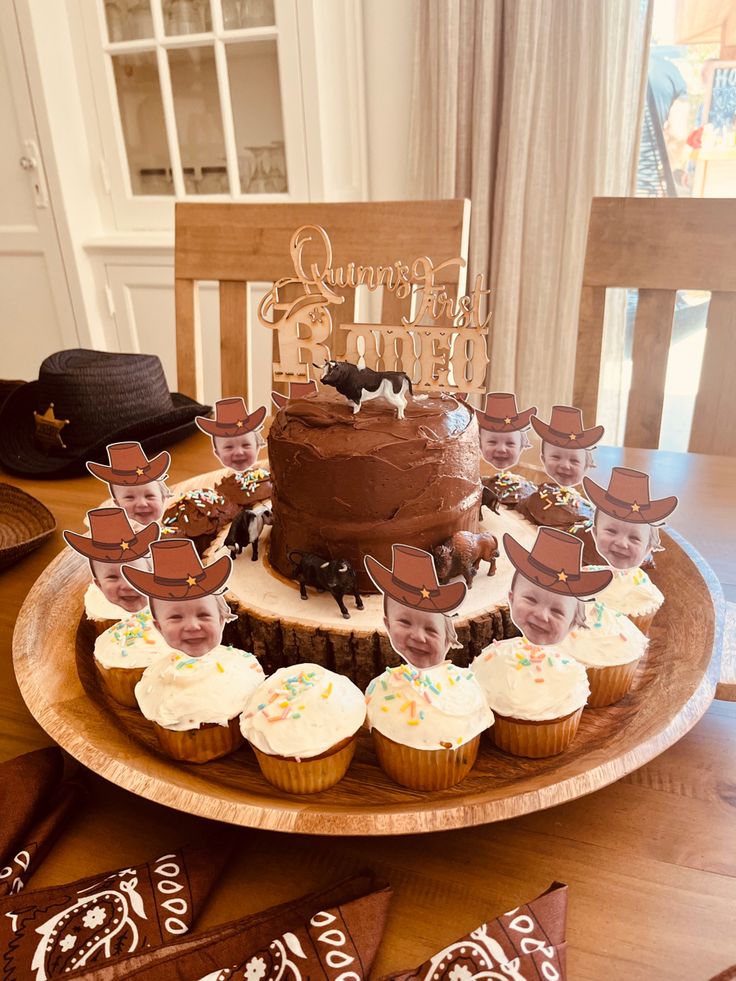 a wooden table topped with cupcakes covered in frosting and cowboy themed decorations