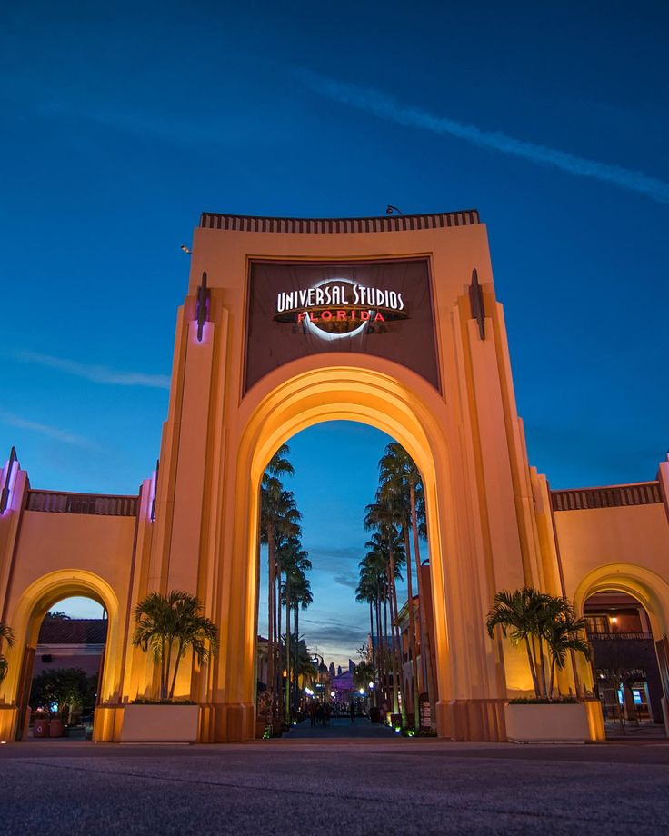 the entrance to universal studios at night with palm trees in the foreground and lights on