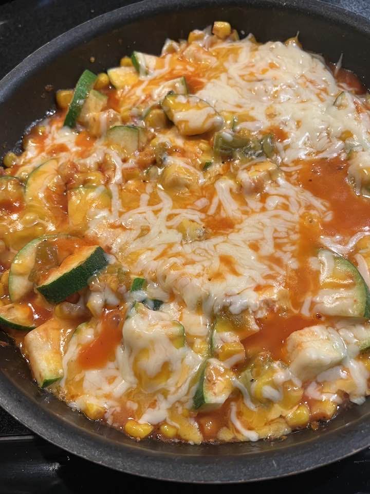 a skillet filled with vegetables and cheese on top of a stove burner next to a frying pan