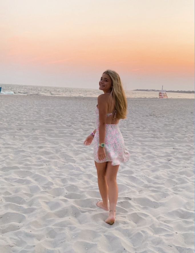 a woman standing on top of a sandy beach next to the ocean in front of a pink sky