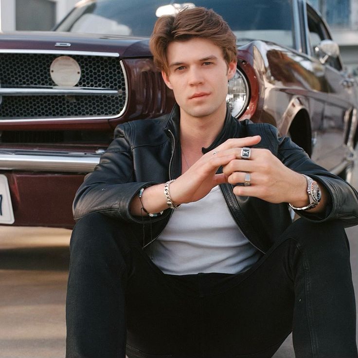 a young man sitting on the ground next to a car