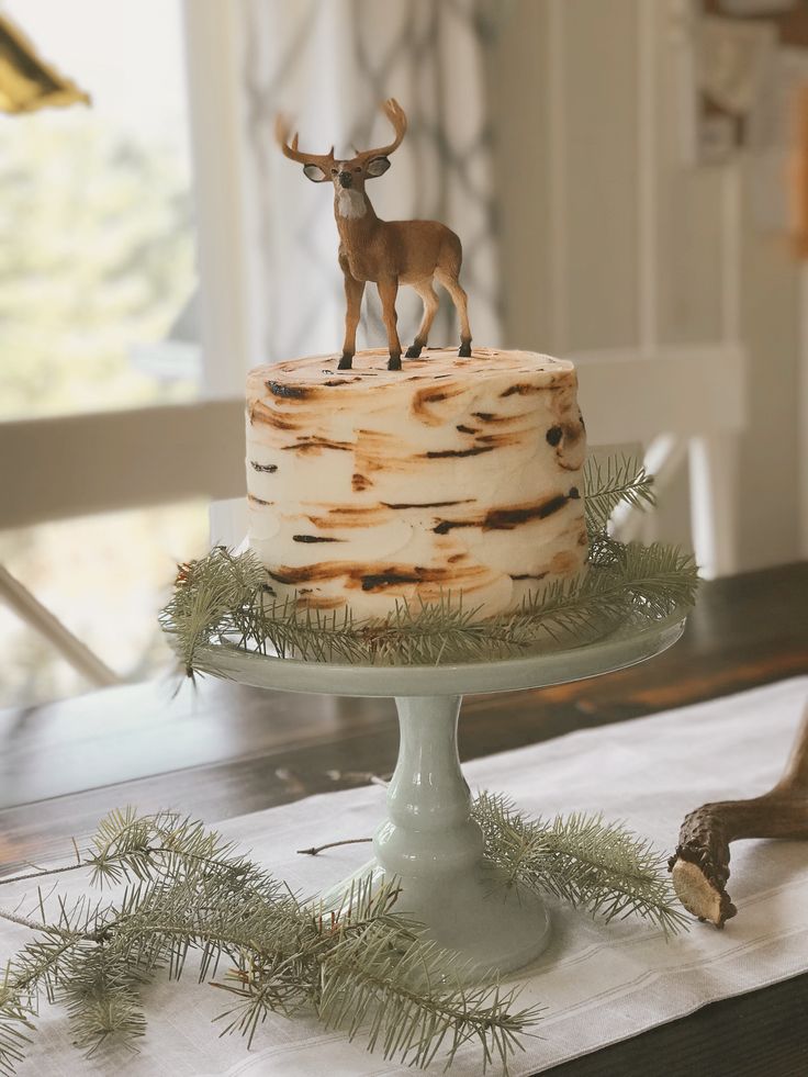 a deer figurine sitting on top of a cake covered in frosting and pine branches