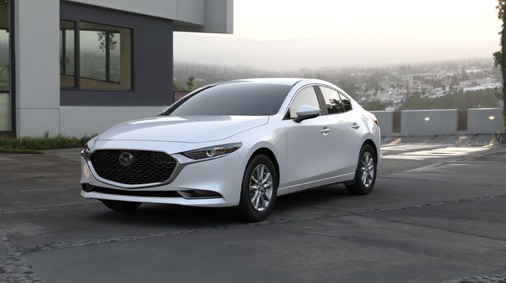 a white mazda car parked in front of a building with mountains in the back ground