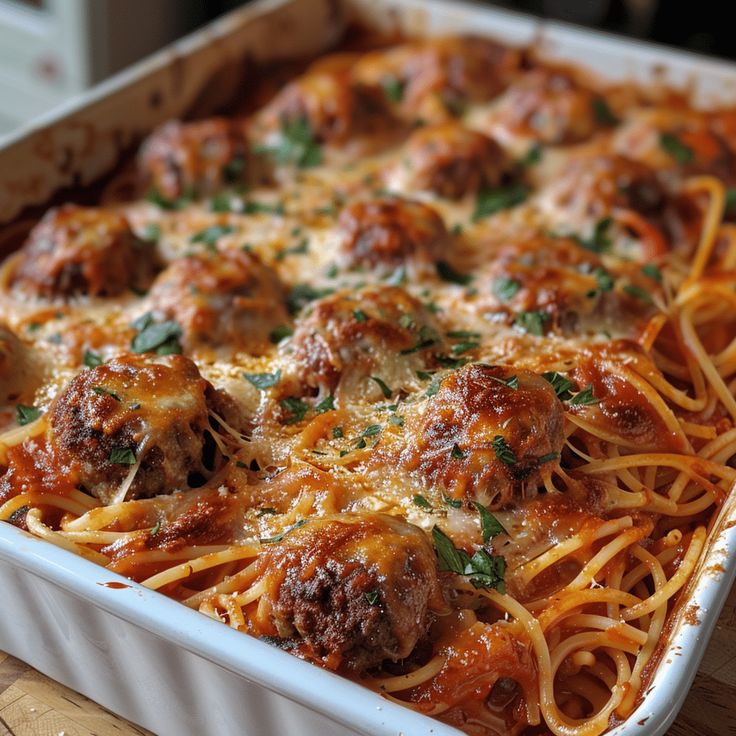 a casserole dish with spaghetti and meatballs in it on a wooden table