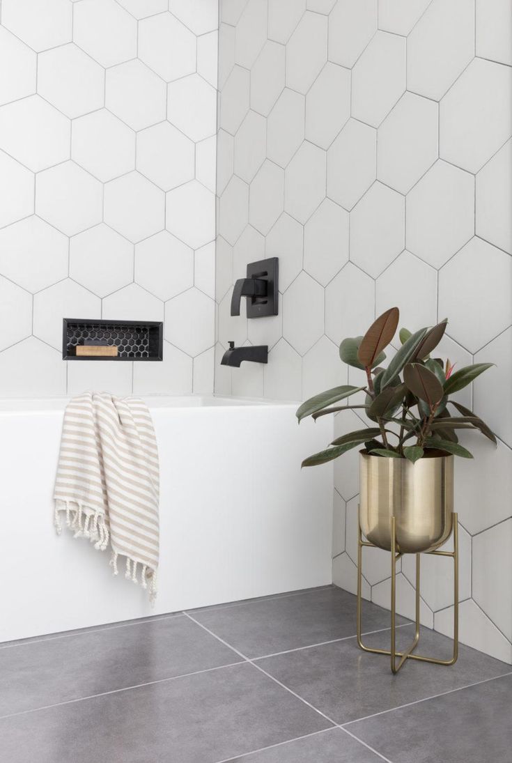 a bathroom with white tiles and gold accents on the bathtub, shower head, and towel rack