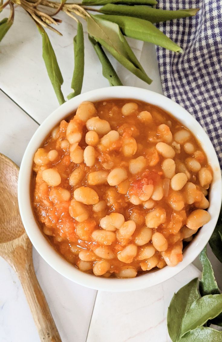 a white bowl filled with beans on top of a table next to some green beans