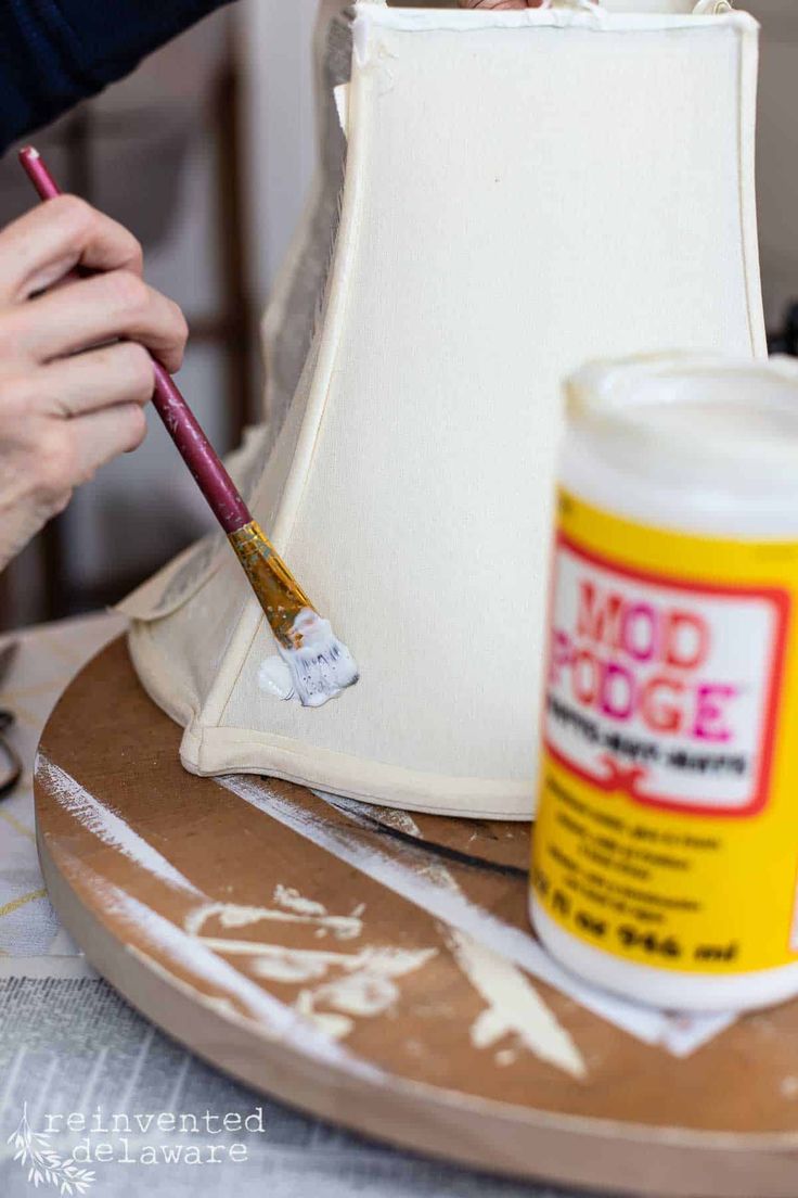 a person is painting a lamp shade on a wooden tray with paint and a brush